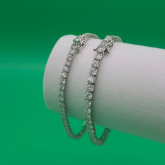 Three diamond bracelets on a white cylindrical stand against a green background