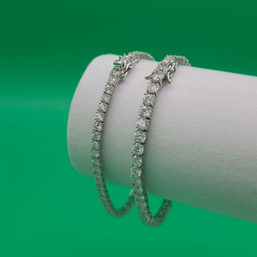 Three diamond bracelets on a white cylindrical stand against a green background